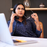 Young indian businesswoman talking on a telephone in an office alone. One female only making a call while looking thoughtful and considering ideas at her desk